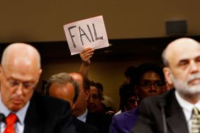 在参议院银行、住房和城市事务委员会举行的听证会上，一名示威者在美国财政部长亨利·保尔森(左)和联邦储备委员会主席本·伯南克(右)身后举着牌子