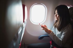 年轻的亚洲女子在商业航班上使用智能手机