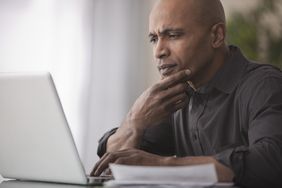 一个人专注地盯着笔记本电脑屏幕，一只手放在键盘上