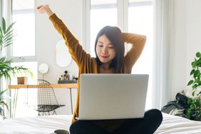 女人盘腿坐着，一边用笔记本电脑一边做伸展运动