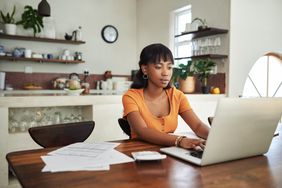 一个女人在家里用笔记本电脑工作，周围都是文件