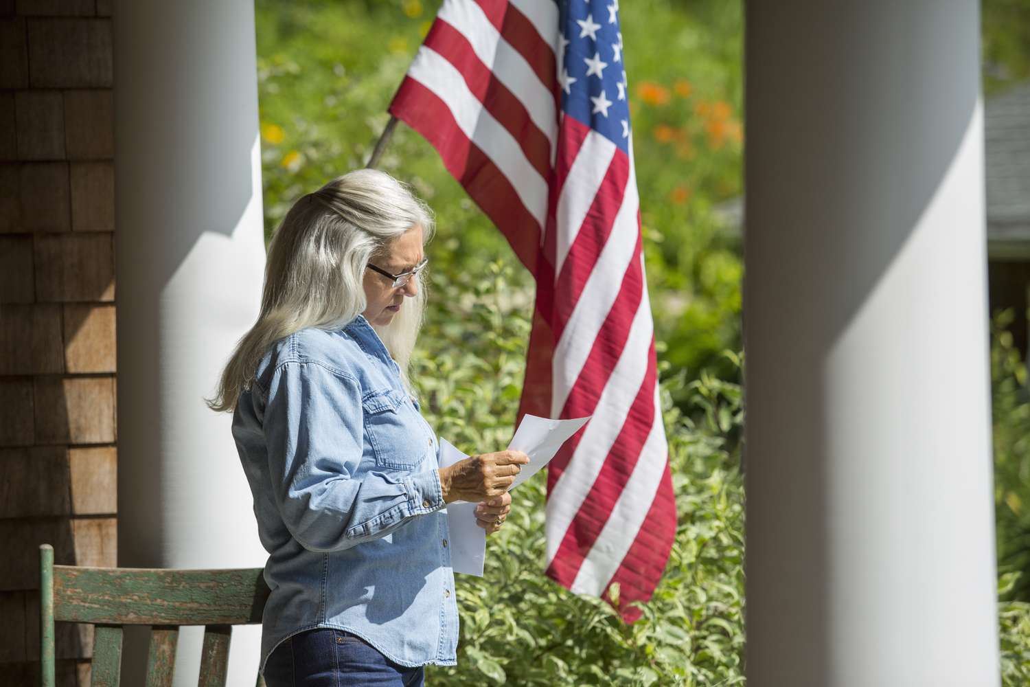 女人站在门廊阅读一封美国国旗的背景。”class=