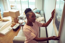 Young girl putting up a painting in her new home