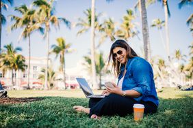 千禧一代企业主在棕榈树环绕的公园里用笔记本电脑工作