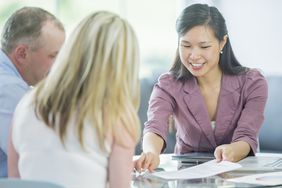 A smiling woman explains the details on a sheet of paper to the couple seated across the desk from her.