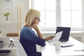 一个金发碧眼的女人在笔记本电脑旁边的桌子上审阅论文