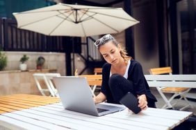 图为一名妇女坐在阳台上用笔记本电脑工作。