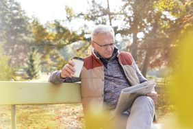 一个老人坐在长凳上喝咖啡看报纸