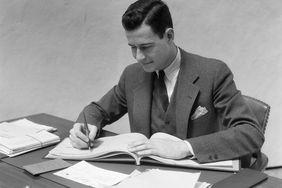 一个20世纪30年代的男人在办公室的桌子上写商业支票簿
