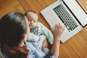 妈妈抱着睡着的宝宝在电脑前工作