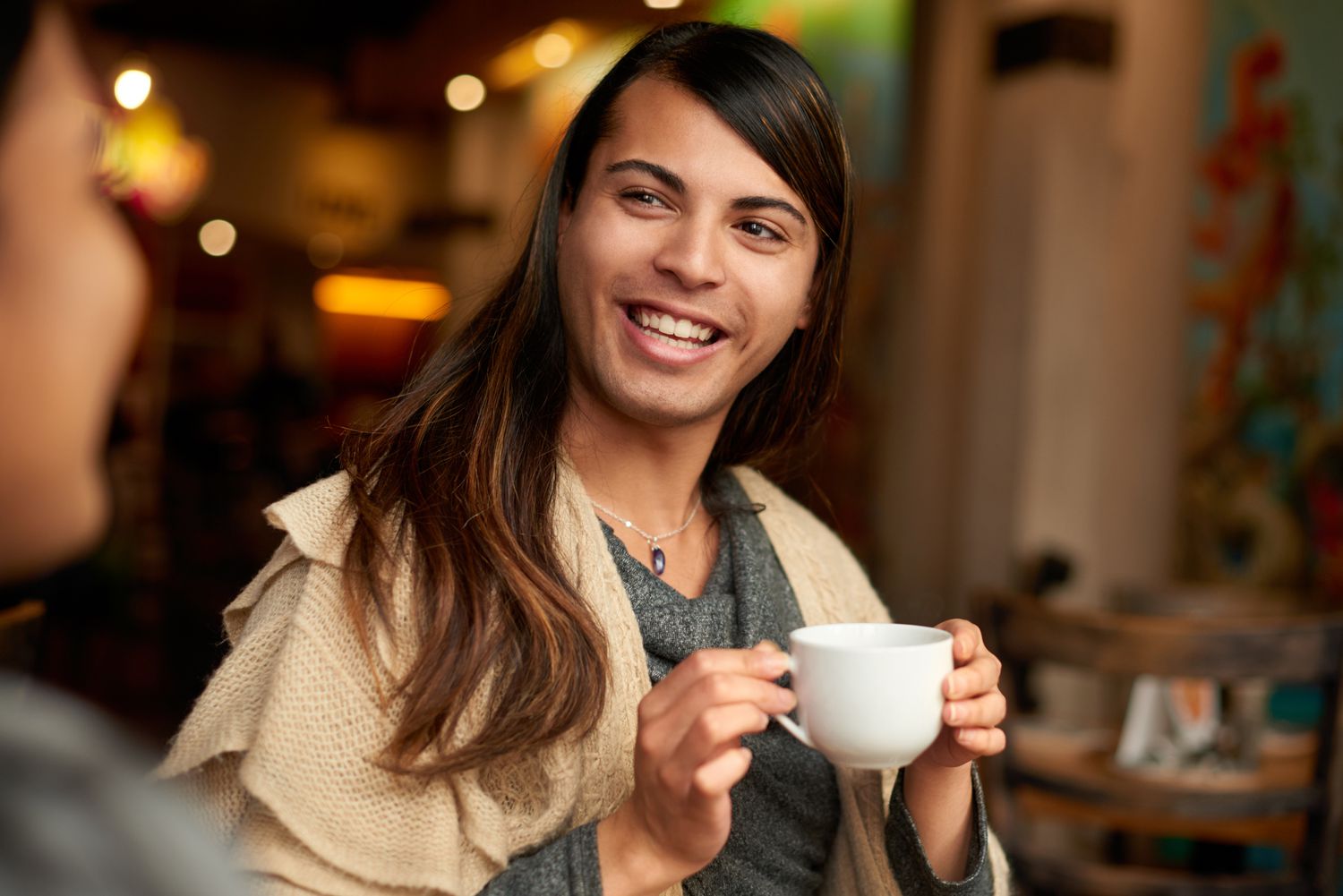 一个性别不固定的人在咖啡馆里喝咖啡时和他们的朋友讨论。