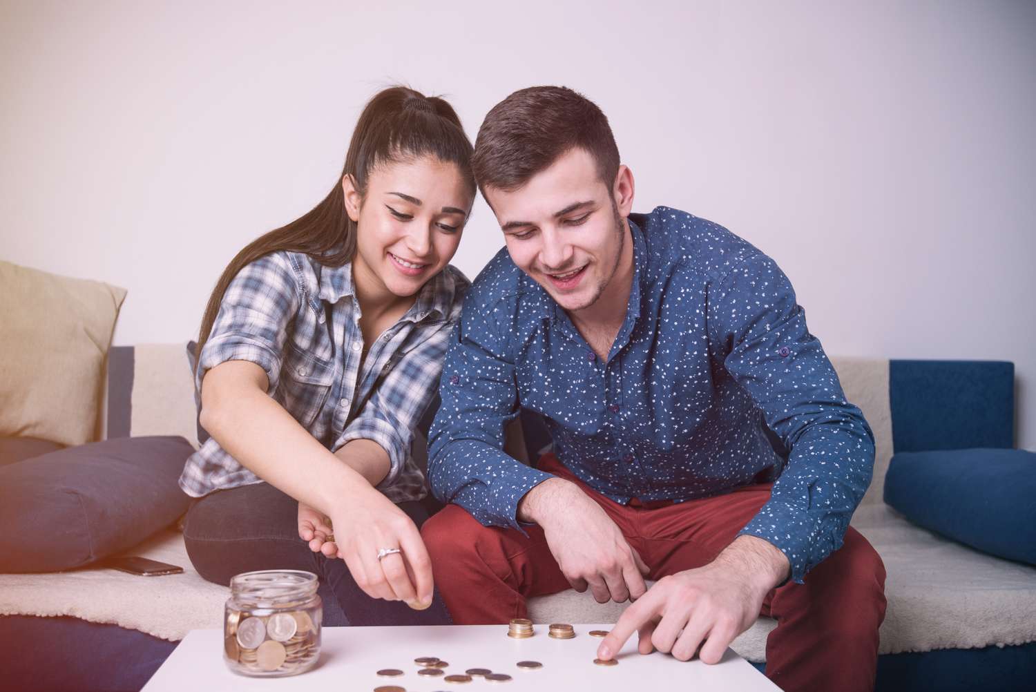 年轻夫妇坐在沙发上数硬币，旁边有一个装满零钱的罐子