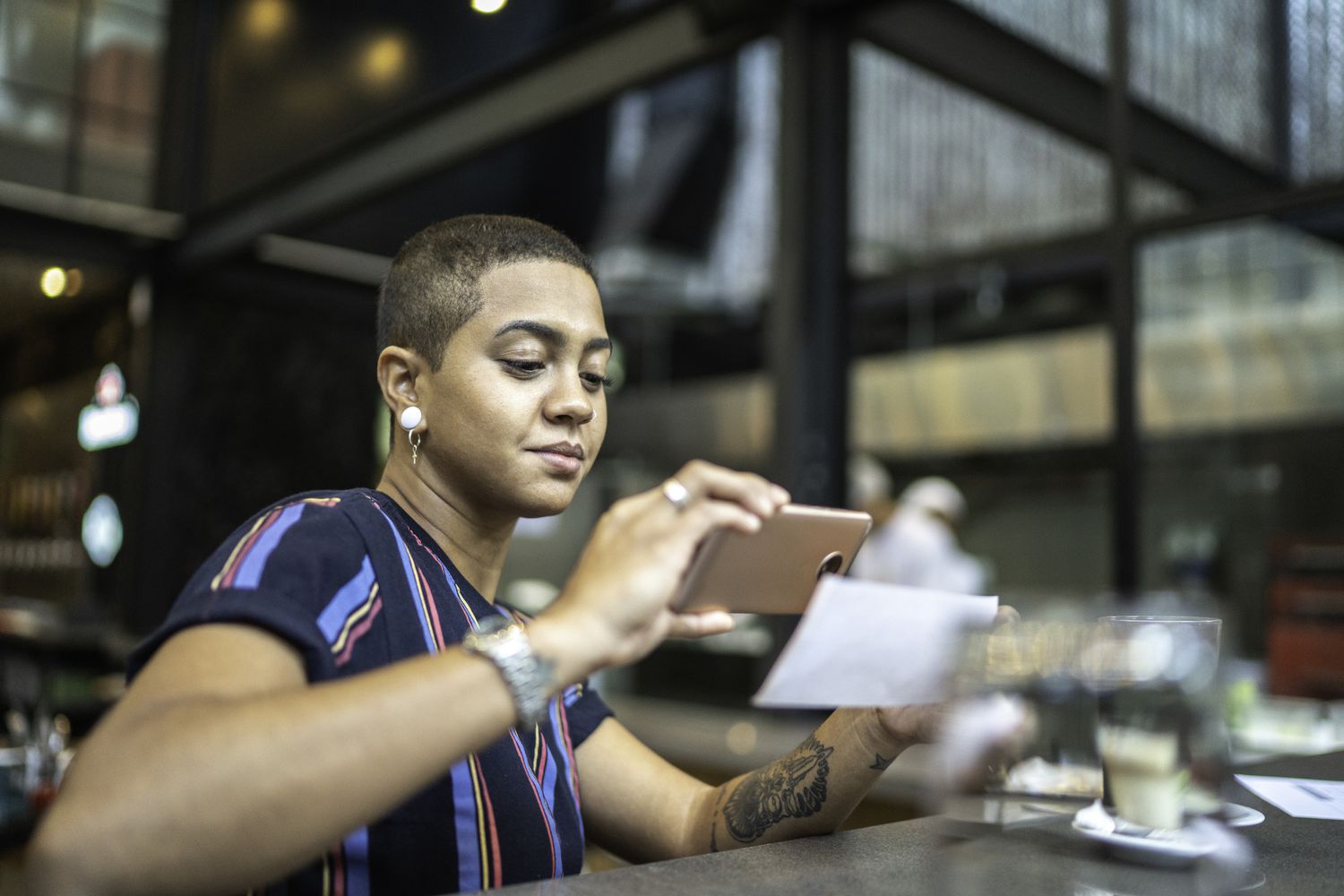一名年轻女子坐在一家户外咖啡馆里，通过智能手机应用程序存入支票。＂class=