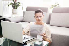 一个女人坐在沙发前拿着笔记本电脑和税务文件