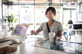 年轻女子在咖啡店柜台使用信用卡读卡器