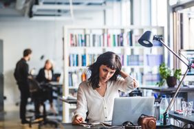 一名女子坐在开放式办公室的办公桌前，盯着笔记本电脑屏幕。