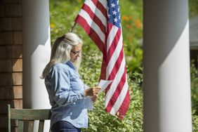一名女子站在门廊前阅读一封信，背景是一面美国国旗。