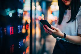 女商人通过证券交易所的屏幕板查看智能手机上的金融交易数据