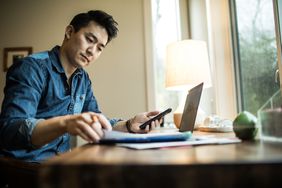 一名坐着的男子在家里用计算器和笔记本电脑计算罗斯个人退休账户存款