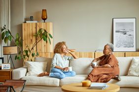 一个年轻的女人和一个年长的女人坐在沙发上聊天，手里拿着咖啡杯