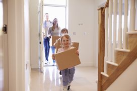 一对夫妇和两个孩子提着箱子穿过新家的前门＂width=