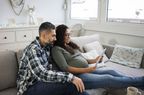 一个留着胡子的男人和一个怀孕的女人坐在沙发上，看着平板电脑上的预算