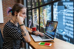 一位年轻女子正在看一台笔记本电脑，背景是股票图表＂>
          </noscript>
         </div>
        </div>
       </div>
       <div class=