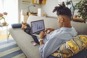 年轻人坐在家里的沙发上用笔记本电脑工作