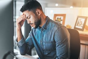 Young adult in jean shirt with hand on his head, stressed out in front of computer