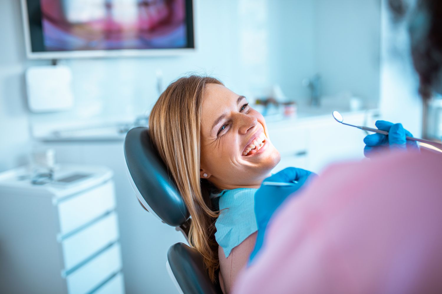 一个女人微笑着坐在牙医的椅子上。＂class=