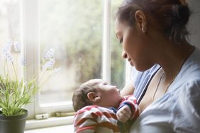 母亲抱着刚出生的婴儿站在窗边