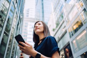一位年轻女子站在摩天大楼前，用手机查看她的投资。＂>
          </noscript>
         </div>
        </div>
       </div>
       <div class=