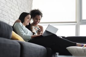 快乐的女同性恋夫妇坐在家里的沙发上网购的低角度视图。