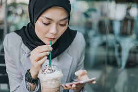 女人一边喝着泡沫咖啡一边用智能手机工作