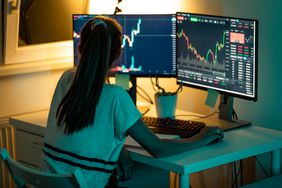 一名妇女在两台电脑显示器上查看股票图表