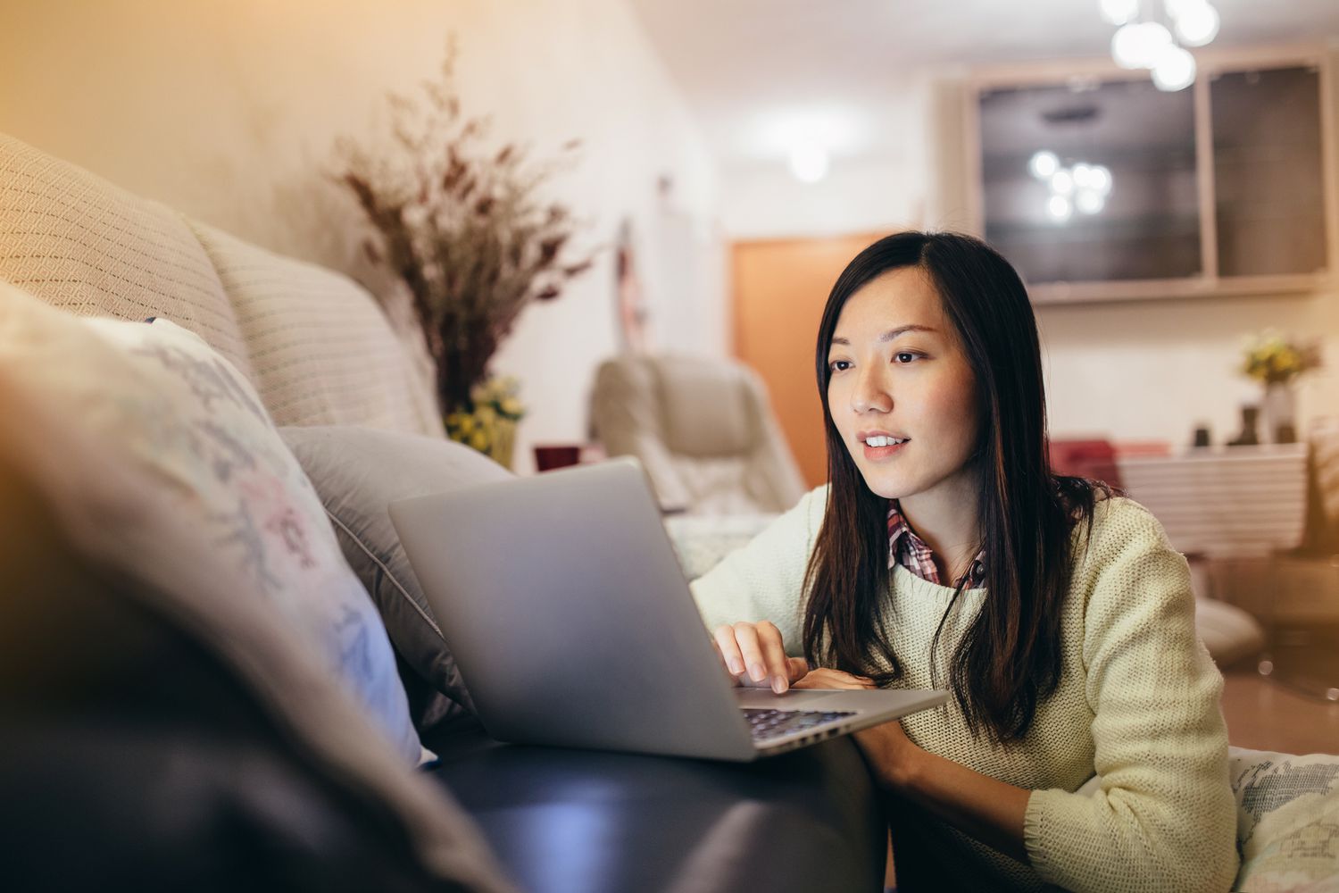 一个女人坐在客厅里，坐在一台打开的笔记本电脑前，双手放在键盘上，专注地看着屏幕
