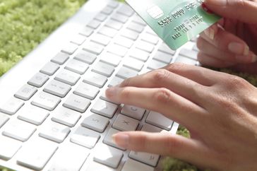 一个人一手在键盘上打字，一手拿着信用卡在网上购物