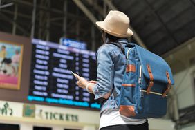 在一个机场候机楼里，一位年轻的背包女游客抬头看着头顶上的航班信息板。