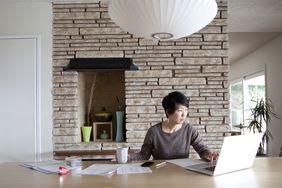 一名妇女在家里的笔记本电脑前喝咖啡，处理财务文书工作