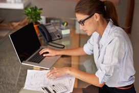 女人看着笔记本电脑和计算器旁边的金融文件＂width=