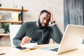 年轻的黑人男子在毛衣看着电脑屏幕在一个紧张的庄园