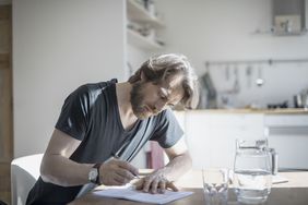 一个人坐在家里写在一个文档和一杯水在他的面前