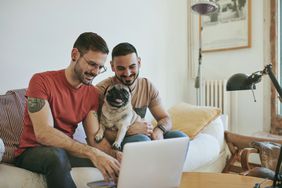 一对夫妇坐在沙发上看着笔记本电脑，手里抱着一只哈巴狗