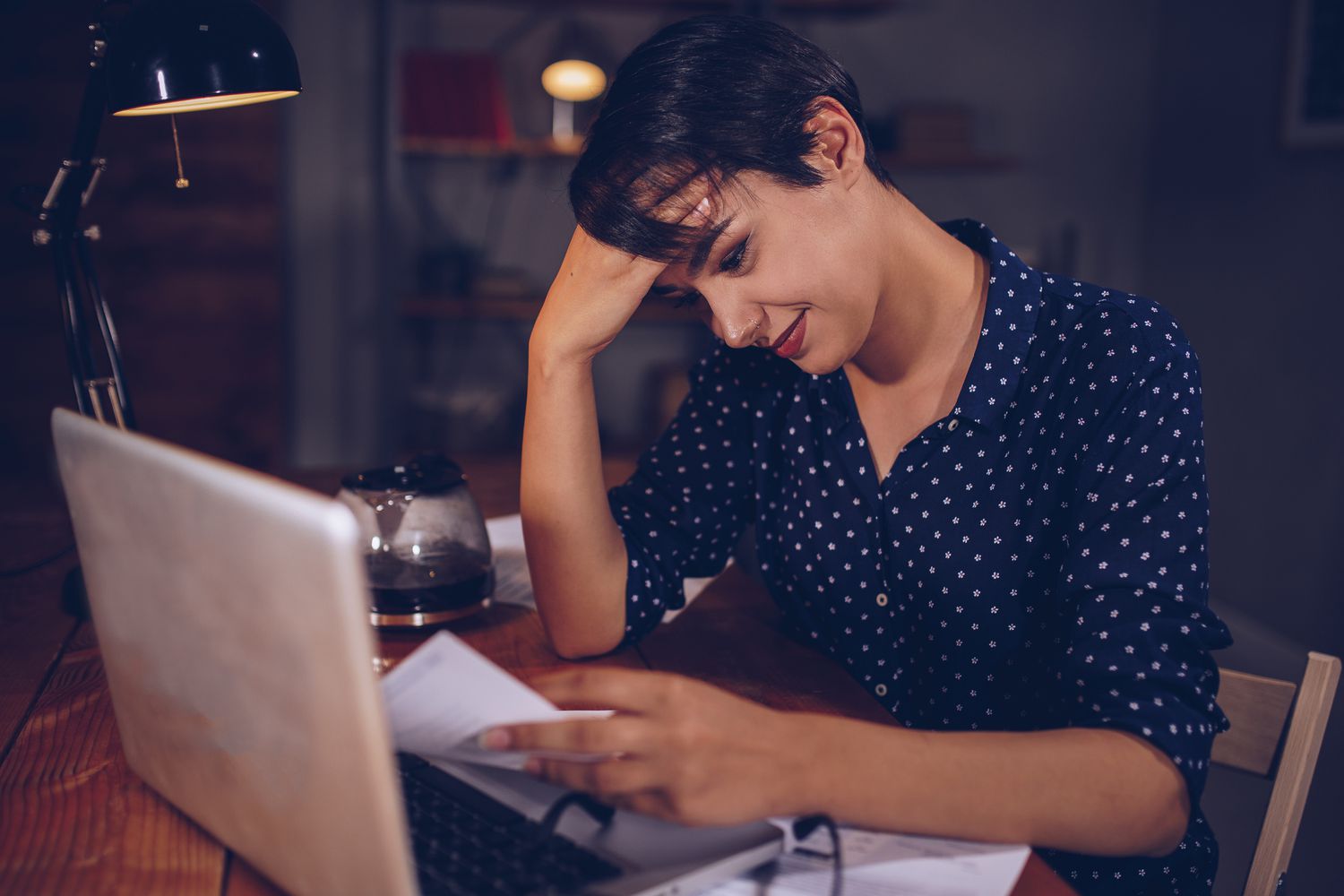 女人坐在桌子前，手放在头上，在笔记本电脑前阅读纳税申报表