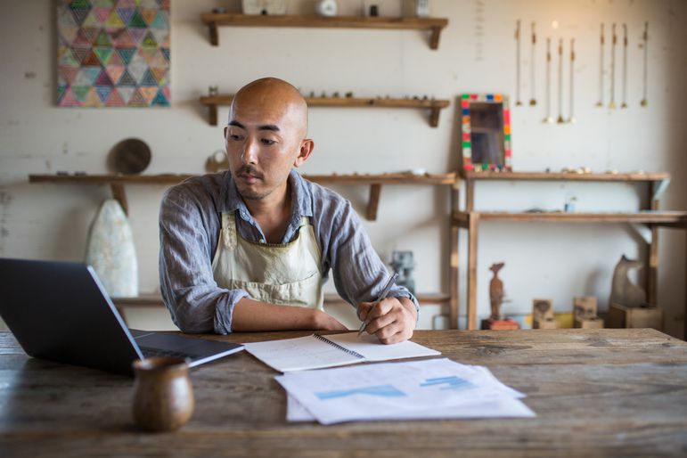 一位企业主坐在他的店里，用他的笔记本电脑和纸查看他的纳税申报表