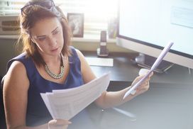 A woman in business attire sits at a desk reviewing documents.