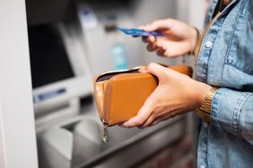 特写:在自动取款机前，一个人左手拿着钱包，右手拿着ATM卡