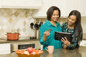 母亲和女儿一起在厨房用平板电脑买东西，母亲拿着信用卡。