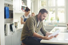 man sitting at counter paying bills while wife and kid are behind him