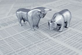 一只牛和一只熊的银色小雕像放在一份印刷好的股市报告上面